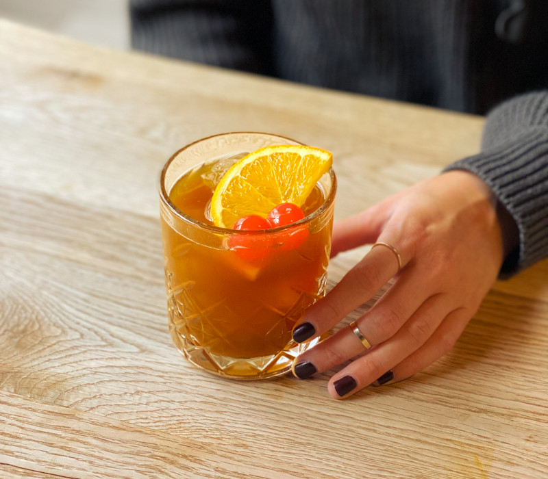 Frau hält Drink mit einer Orangenscheibe in der Hand