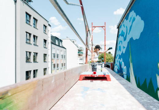 Eine Frau auf einem Gerüst arbeitet an einem Grafitti