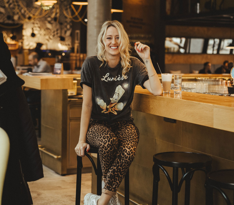 Lachende Frau sitzt mit einem Kaffee an Schani's Bar