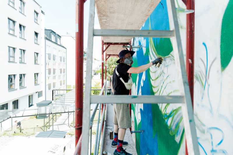 Ein Künstler auf einem Gerüst arbeitet an einem Grafitti