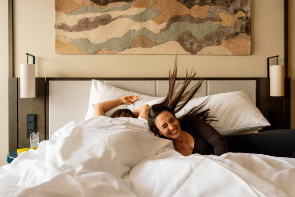 Eine lächelnde Frau lässt sich in ihr Bett im Hotelzimmer fallen
