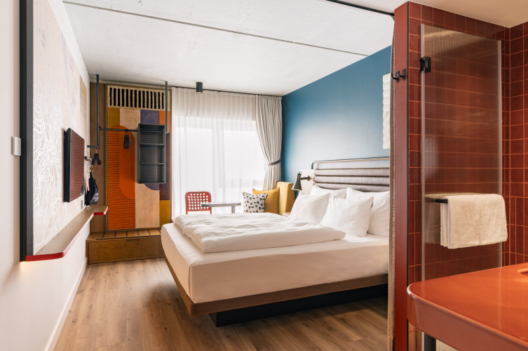 Doppelbett, Fernseher und offener Schrank in einem hellen Zimmer im Hotel Schani Naschmarkt
