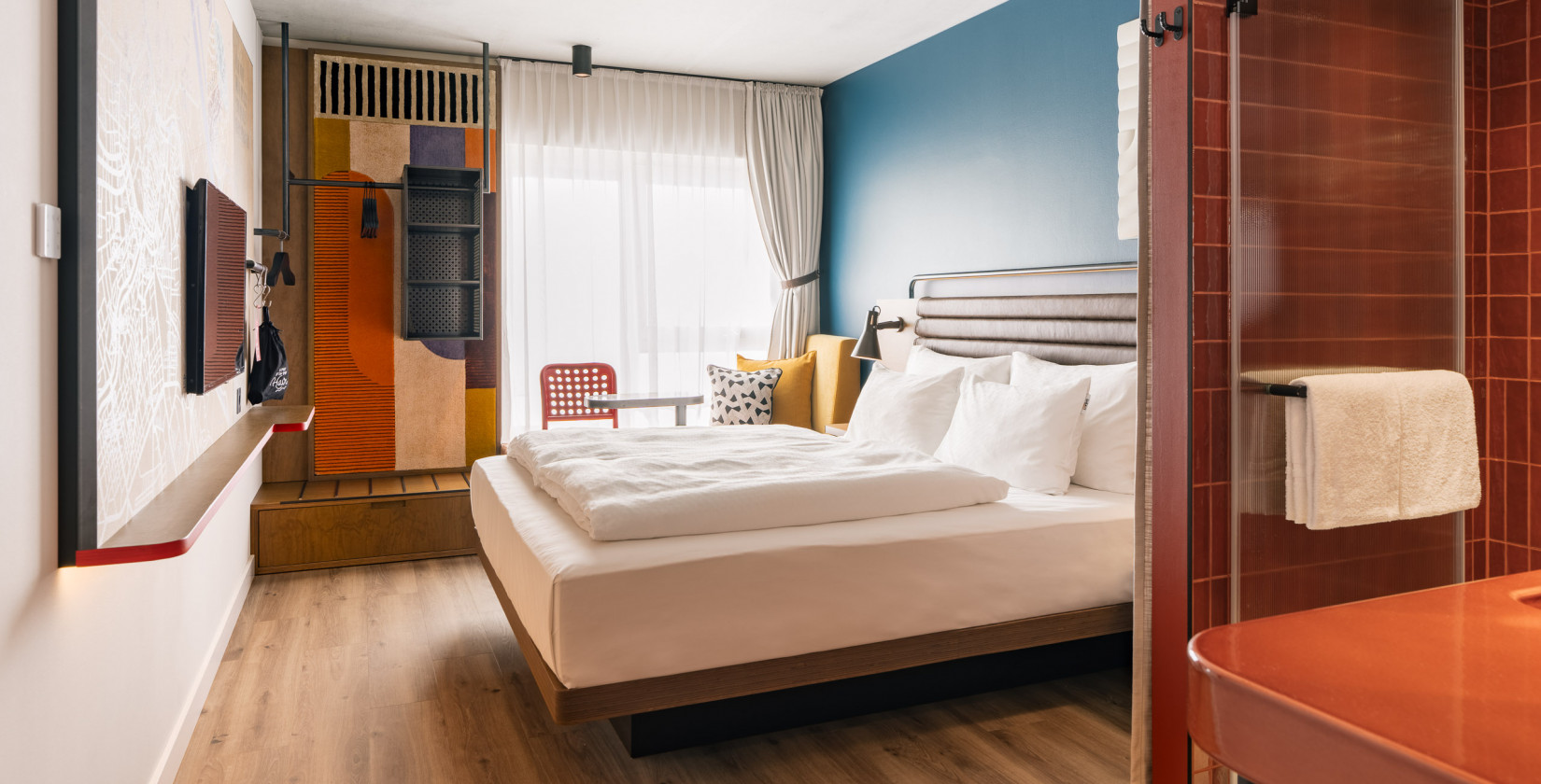 Hotelzimmer mit großzügigem Doppelbett, Fernseher und offenem Kleiderschrank