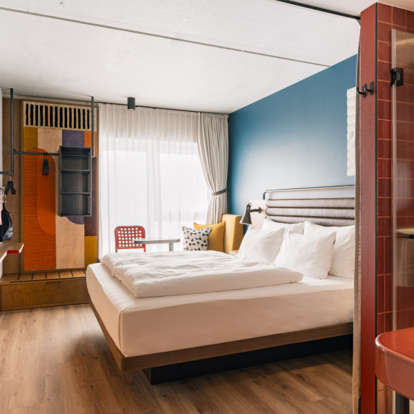 Doppelbett neben einer gepolsterten Fensterbank und einem offenen Kleiderschrank im Hotel Schani Naschmarkt