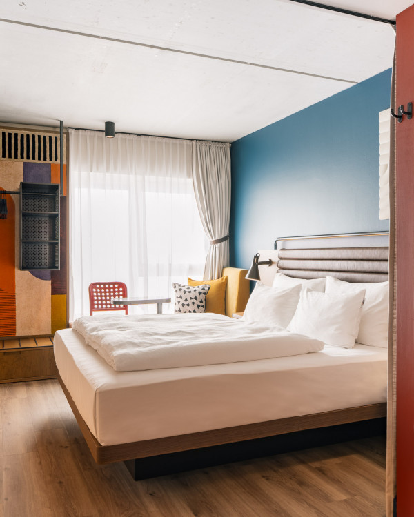 Doppelbett neben einer gepolsterten Fensterbank und einem offenen Kleiderschrank im Hotel Schani Naschmarkt