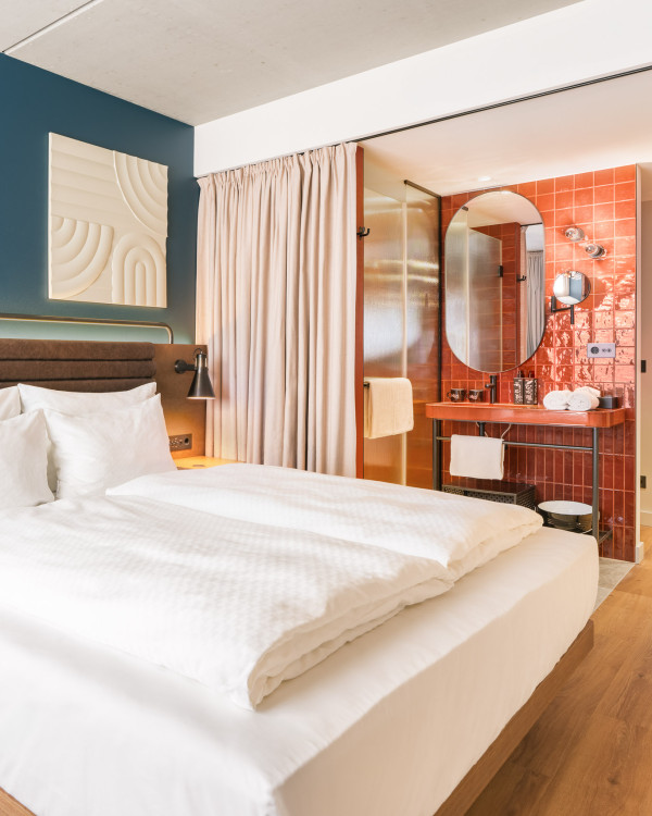 Doppelbett, offenes Badezimmer mit Regendusche und Waschtisch in einem Smart Garden Zimmer