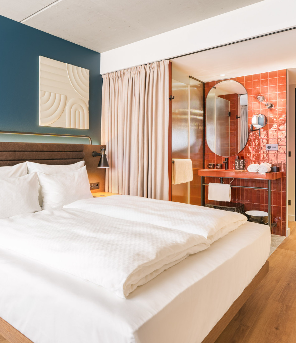 Doppelbett, offenes Badezimmer mit Regendusche und Waschtisch in einem Smart Garden Zimmer