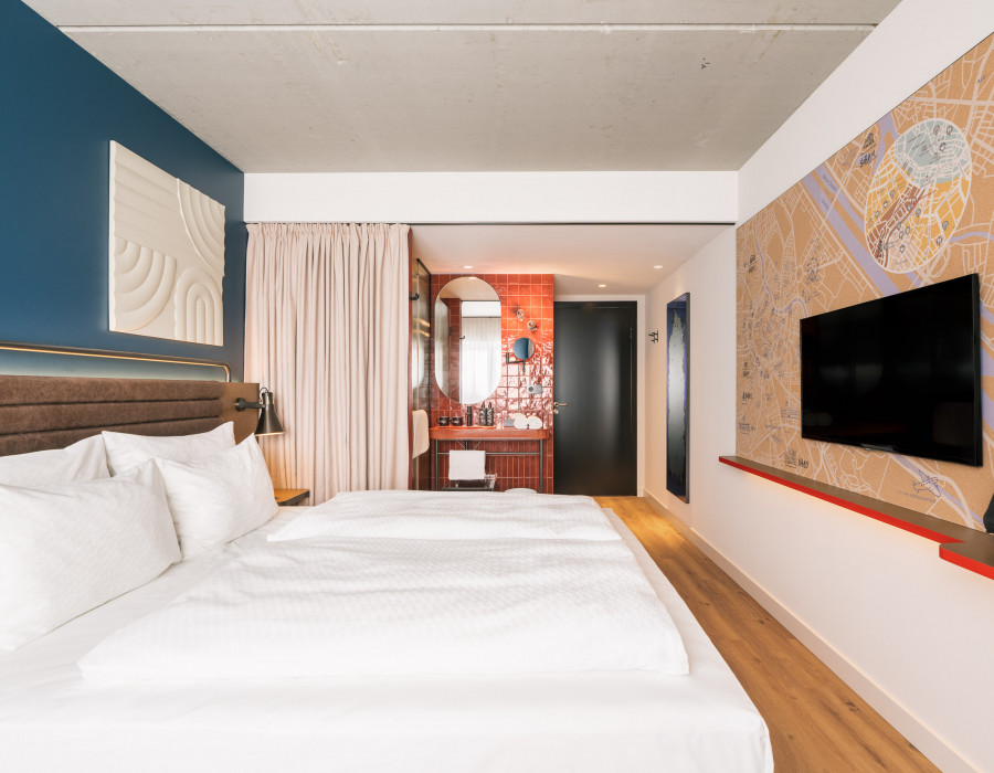 Doppelbett, TV, Stadtplan von Wien an einer Wand und ein offenes Badezimmer im Hotel Schani Naschmarkt