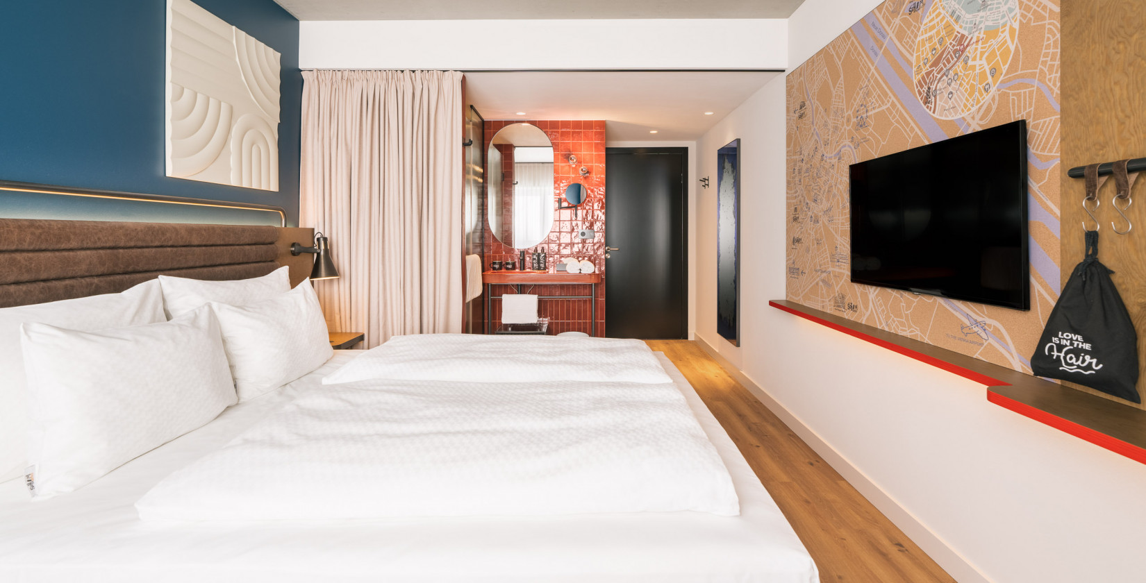 Doppelbett und offenes Badezimmer mit Waschtisch und Regendusche in einem Zimmer im Hotel Schani Naschmarkt