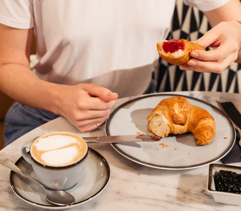 Frau frühstückt Croissants mit Marmelade und Milchkaffee im Hotel im Wiener Zentrum 