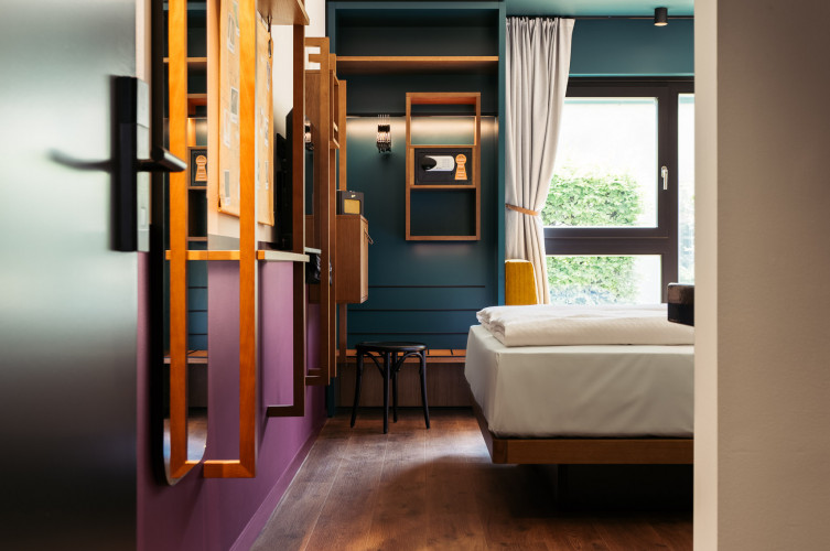 Blick ins Smart Street Zimmer mit Doppelbett, offenem Kleiderschrank und Sitzbank beim Fenster