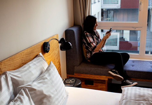 Frau sitzt am Fenster im Hotelzimmer im Hotel Schani und schaut auf ihr Handy