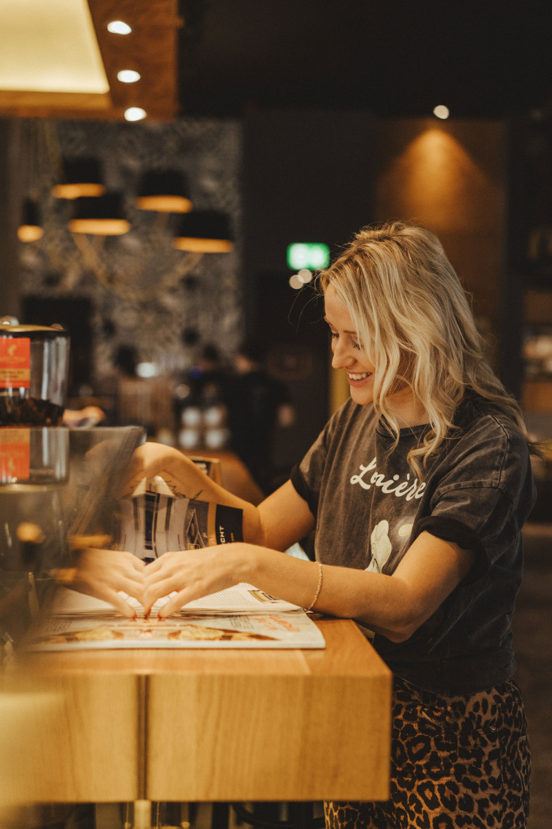 Frau blättert in Zeitung an Schani's Bar