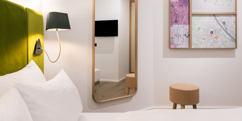 Spiegel, Doppelbett und kleiner Hocker im Smart Economy Zimmer im Bio-Hotel Schani Wienblick