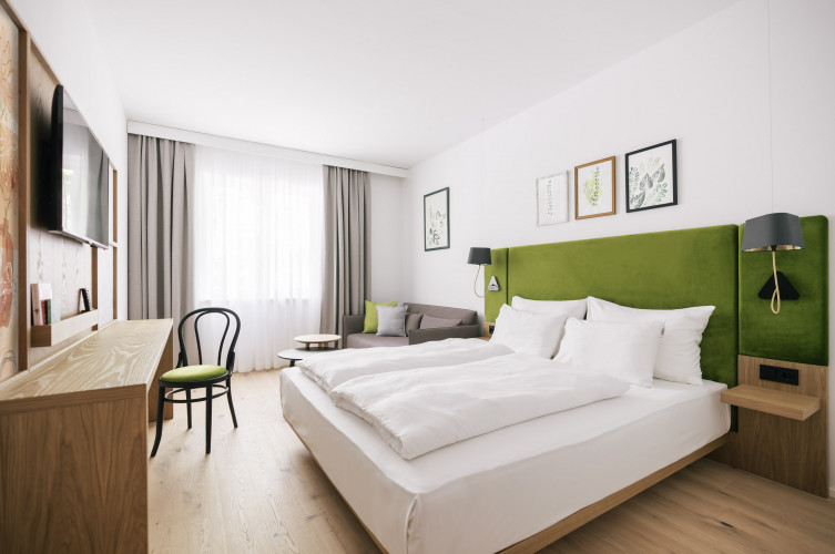 Double Bed, pull out sofa, table and chair with a TV on the wall at Bio-Hotel Schani Wienblick