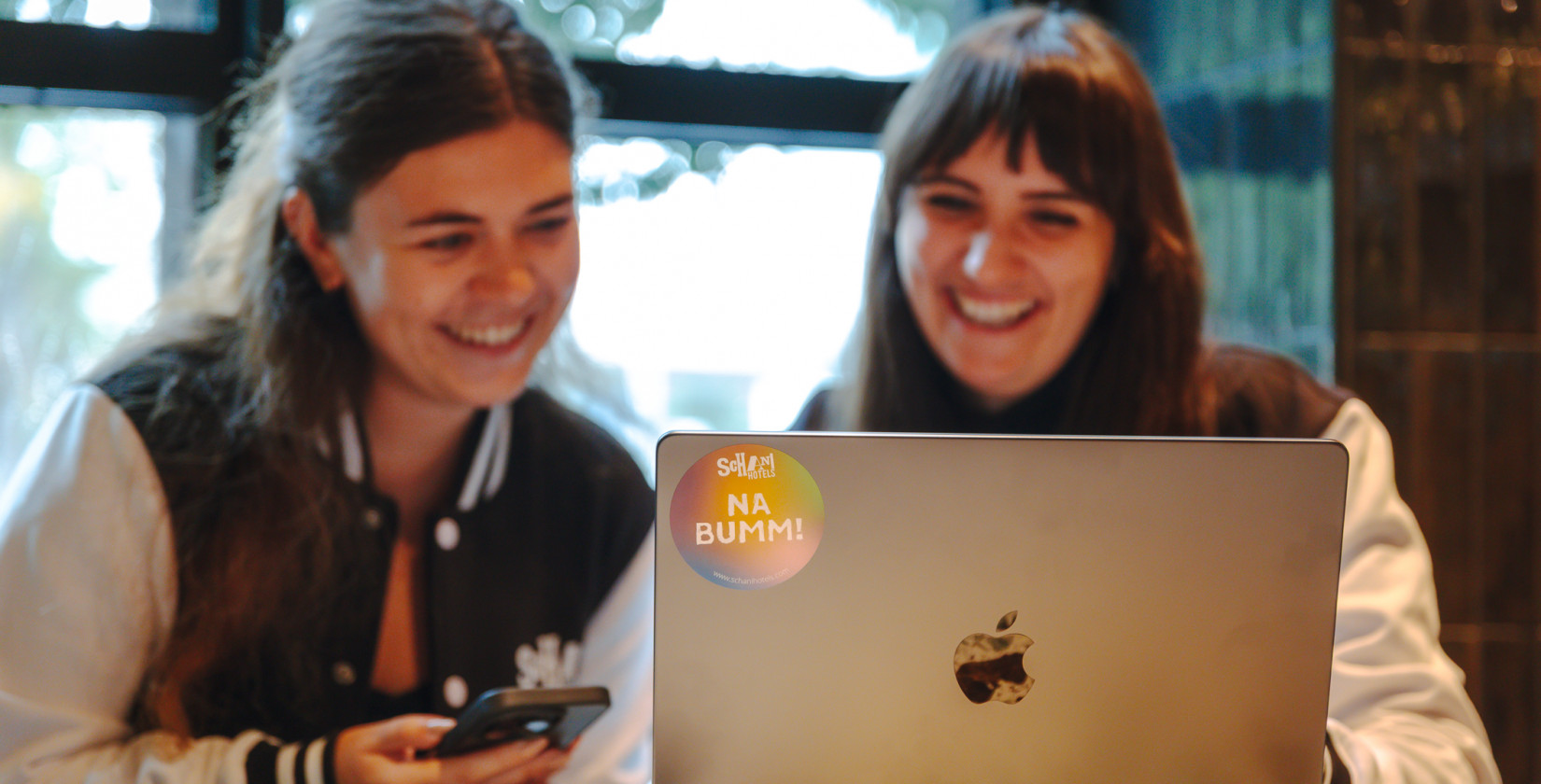 Zwei lächelnde Frauen sitzen vor einem Laptop