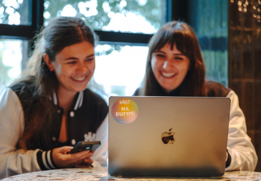 Zwei lächelnde Frauen sitzen vor einem Laptop