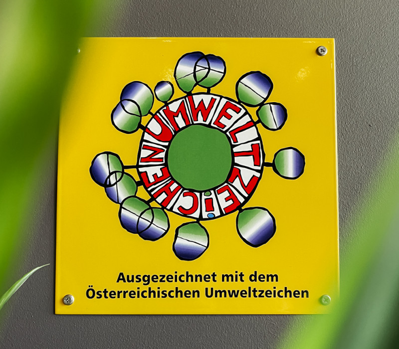 Gelbes Schild an einer grauen Wand informiert über die Auszeichnung mit dem Österreichischen Umweltzeichen