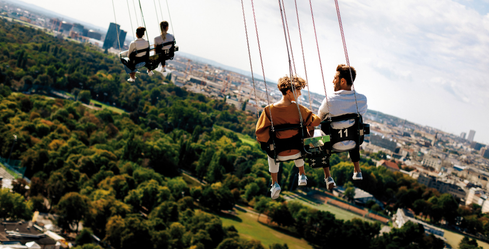 Vier Menschen bei der Fahrt mit dem Kettenkarussell im Wiener Prater mit Blick über die Stadt. 